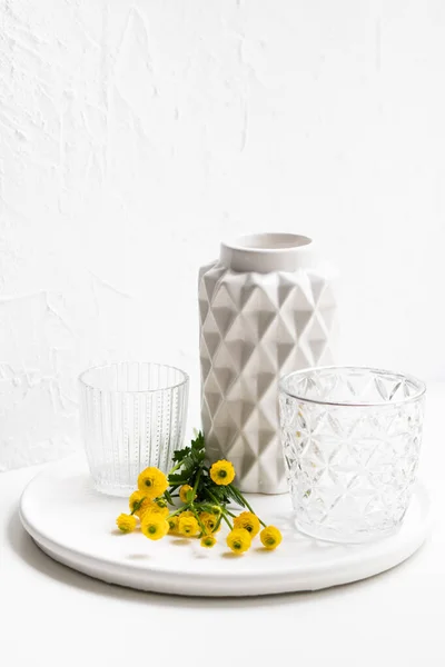 Witte huisdecoratie met gele bloemen, keramische vaas en glas op dienblad — Stockfoto