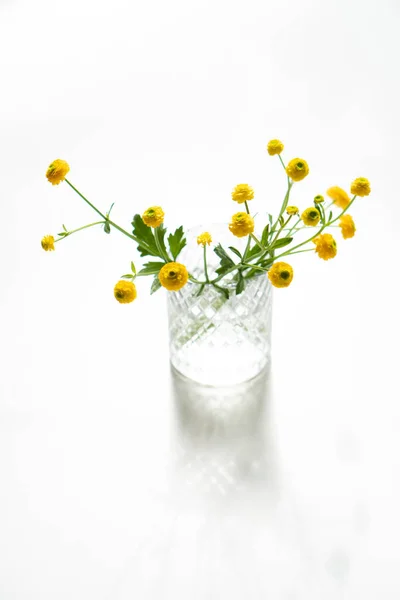 Kleine gele boterbloemen in glazen vaas — Stockfoto