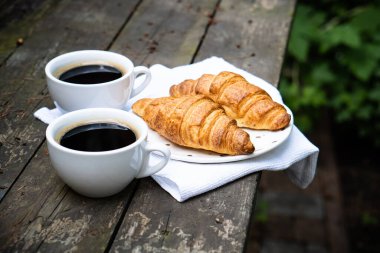 Eski ahşap masada kahve ve kruvasan.