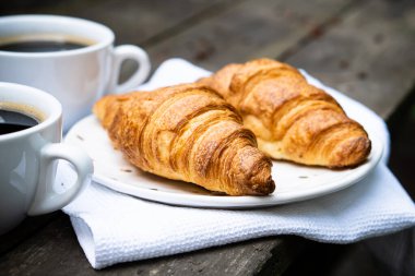 Eski ahşap masada kahve ve kruvasan.