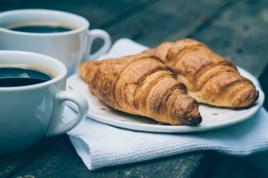 Eski ahşap masada kahve ve kruvasan.