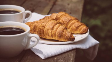 Eski ahşap masada kahve ve kruvasan.