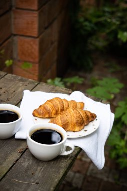 Eski ahşap masada kahve ve kruvasan.