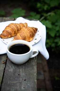 Eski ahşap masada kahve ve kruvasan.