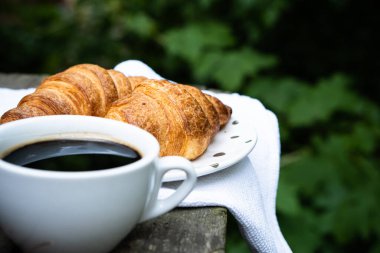 Eski ahşap masada kahve ve kruvasan.