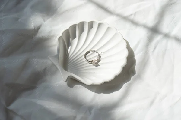 带纹理亚麻布背景的贝壳形珠宝镶板上的订婚戒指 — 图库照片