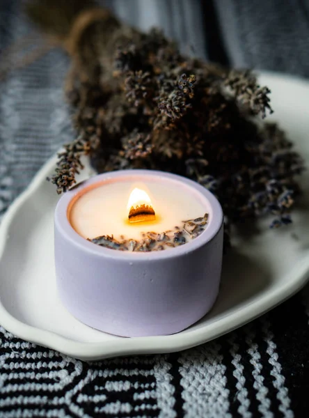 Hořící levandulově vonící svíčka s dřevěným knotem a svazkem sušených bylin na bílém keramickém podnosu — Stock fotografie