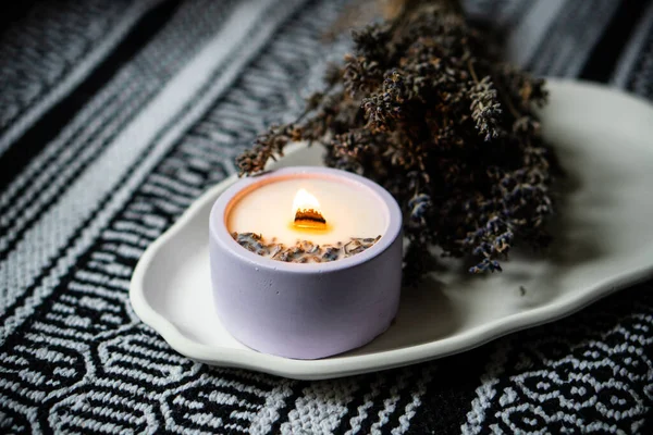 Brennende Lavendelduftkerze mit Holzdocht und Bündel getrockneter Kräuter auf weißem Keramiktablett — Stockfoto
