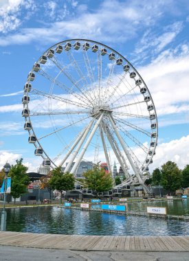 Kanada, Montreal - 11 Temmuz 2021: Montreal 'in Eski Limanı' ndaki La Grande Roue de Montreal dönme dolabının mavi gökyüzü ve bulutların üzerindeki manzarası. Montreal 'in eski limanı Quebec' in tarihi limanıdır..
