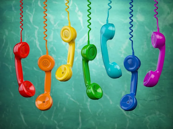 Telehone receivers of different colors hanging on the green back — Stock Photo, Image