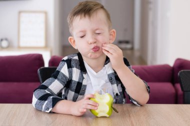 Çocuk oturma odasındaki masada yeşil elma yiyor..