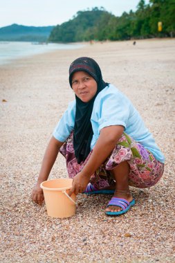 Musilim woman collecting shells on a beach.