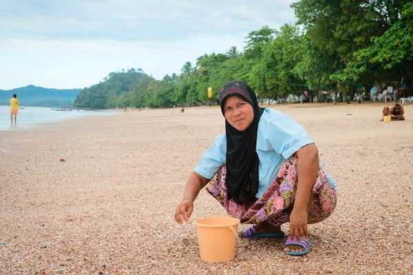 Musilim woman collecting shells on a beach.