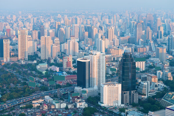 Many highrise buildings of Bangkok Thailand's crowded, urban skyline, in the hazy, early morning light, from an elevated perspective.