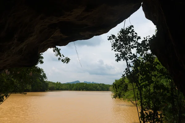 Ciel nuageux au-dessus d'une rivière boueuse depuis l'intérieur d'une grotte — Photo