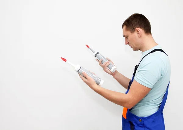 Young worker reading ingredients on silicone sealant bottle — Stock Photo, Image