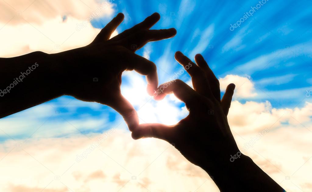 Silhouette hands in heart shape and blue sky