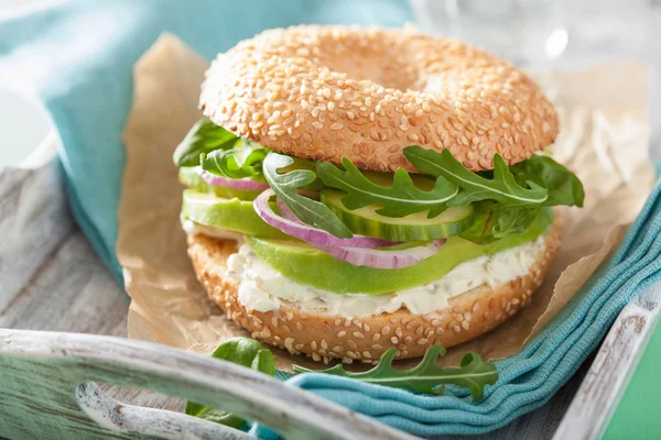 Avocado sandwich på bagel med flødeost løg agurk arugu - Stock-foto