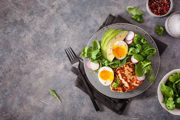 Sağlıklı keto paleo diyeti kahvaltısı: haşlanmış yumurta, avokado, halloumi peyniri, salata yaprakları.