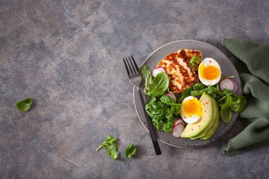 Sağlıklı keto paleo diyeti kahvaltısı: haşlanmış yumurta, avokado, halloumi peyniri, salata yaprakları.