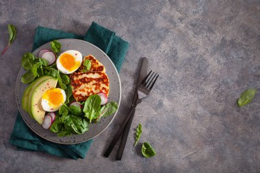 Sağlıklı keto paleo diyeti kahvaltısı: haşlanmış yumurta, avokado, halloumi peyniri, salata yaprakları.