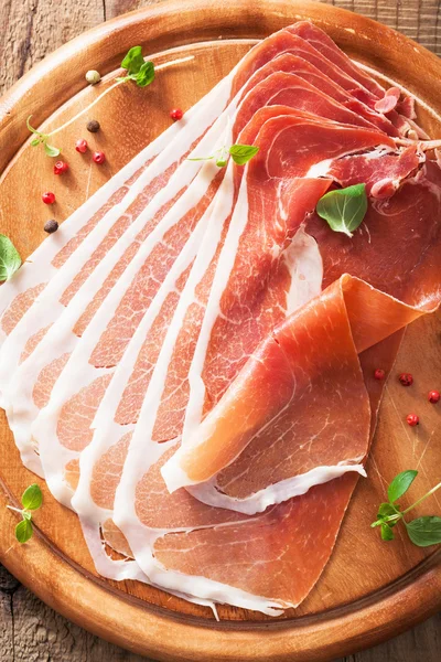 Sliced prosciutto ham on chopping board with oregano and pepper — Stock Photo, Image