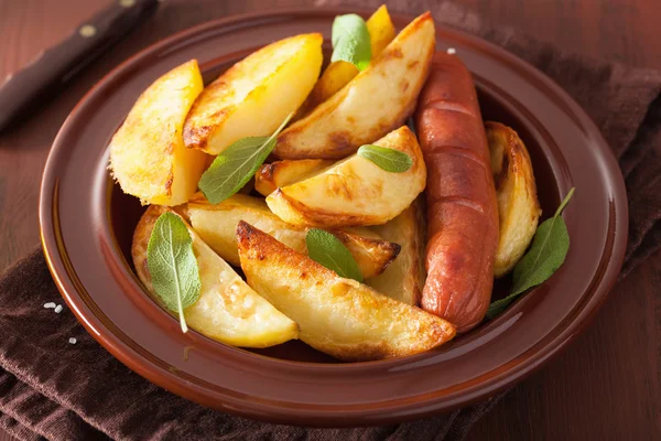 Baked potato wedges and sausage in plate over brown rustic table — Stock Photo, Image