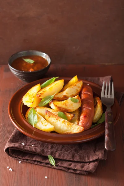 Cuñas de patata al horno y salchichas en plato sobre mesa rústica marrón —  Fotos de Stock