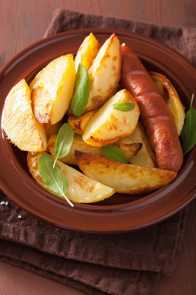 Cuñas de patata al horno y salchichas en plato sobre mesa rústica marrón —  Fotos de Stock