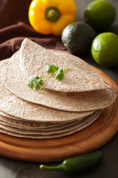 Whole wheat tortillas on wooden board and vegetables — Stock Photo, Image