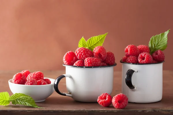 Frische Himbeere in Emaille-Tassen über Holzhintergrund — Stockfoto