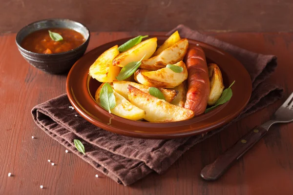 Baked potato wedges and sausage over brown rustic table — Stock Photo, Image