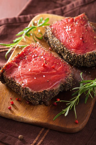 Bife cru com especiarias e alecrim sobre fundo de madeira — Fotografia de Stock