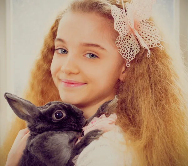 Красивая маленькая девочка сидит на подоконнике и играет с пасхальным кроликом . — стоковое фото