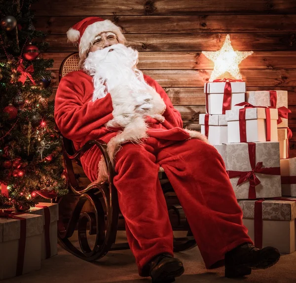 Санта Клаус сидит на кресле-качалке в интерьере деревянного дома — стоковое фото
