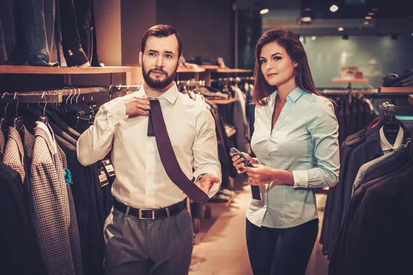 Confident handsome man with beard choosing a tie in a suit shop. — Stock Photo, Image