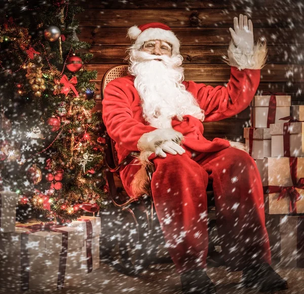 Weihnachtsmann sitzt auf Schaukelstuhl im hölzernen Hausinneren — Stockfoto