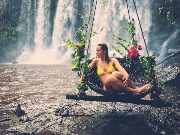 Belle femme assise dans une balançoire fleurie près d'une cascade — Photo