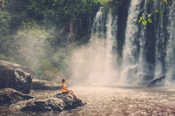 Beautiful woman sitting near waterfall — Stock Photo, Image