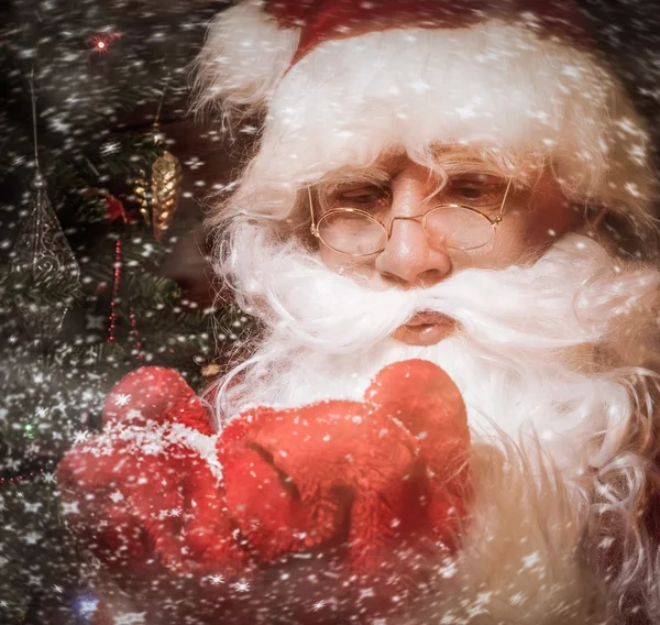 Papai Noel em casa de madeira interior soprando neve de suas mãos — Fotografia de Stock