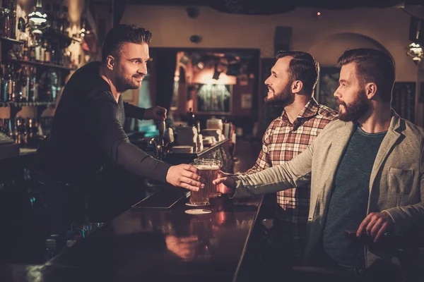 friends drinking draft beer at bar counter in pub.