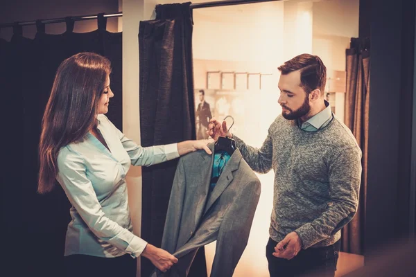 Självsäker vacker man med skägg att välja en jacka i en kostym butik. — Stockfoto