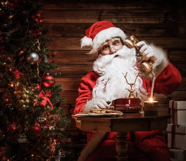 Санта-Клаус разговаривает по телефону в деревянном интерьере дома — стоковое фото