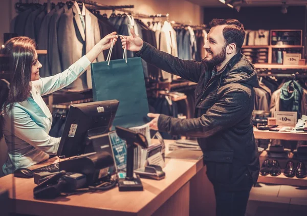 Joyeux bel homme prenant sac à provisions de vendeuse dans un magasin de costumes . — Photo