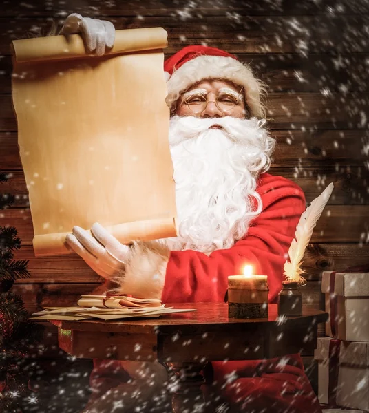 Santa claus v dřevěných domů interiéru čtení seznamu přání svitek — Stock fotografie