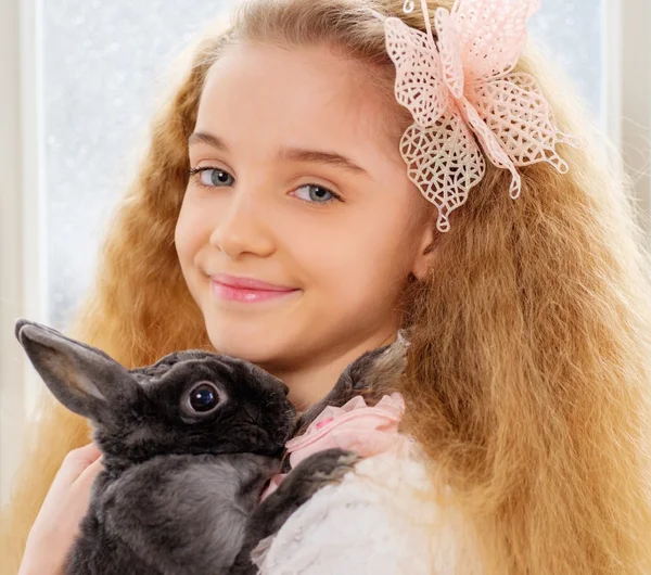 Hermosa niña sentada en un alféizar de la ventana y jugando con el conejo de Pascua . —  Fotos de Stock