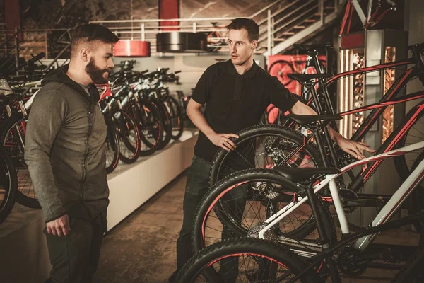 Vendedor mostrando uma nova bicicleta para o cliente interessado na loja de bicicletas . — Fotografia de Stock