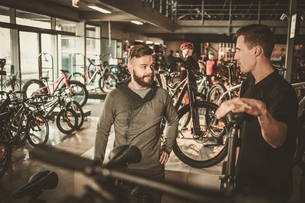 Sprzedawca pokazuje nowy rower do zainteresowanych klientów w sklepie rowerowym. — Zdjęcie stockowe