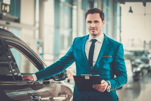 Jovem concessionário de automóveis em pé no showroom . — Fotografia de Stock