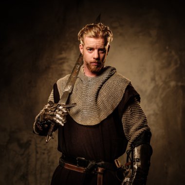 Young medieval knight posing on dark background.  clipart